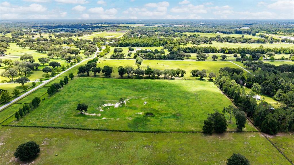 An aerial view shows a large, fenced grassy pasture with scattered trees and surrounding rural landscape — SE 159TH LN., SUMMERFIELD, FL