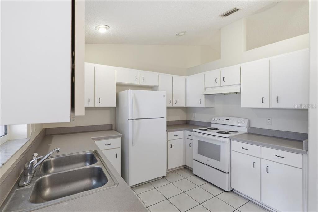 A kitchen with white cabinets, white appliances, gray countertops, and white tile flooring — 4 PONY LANE UNIT A & B, PALM COAST, FL