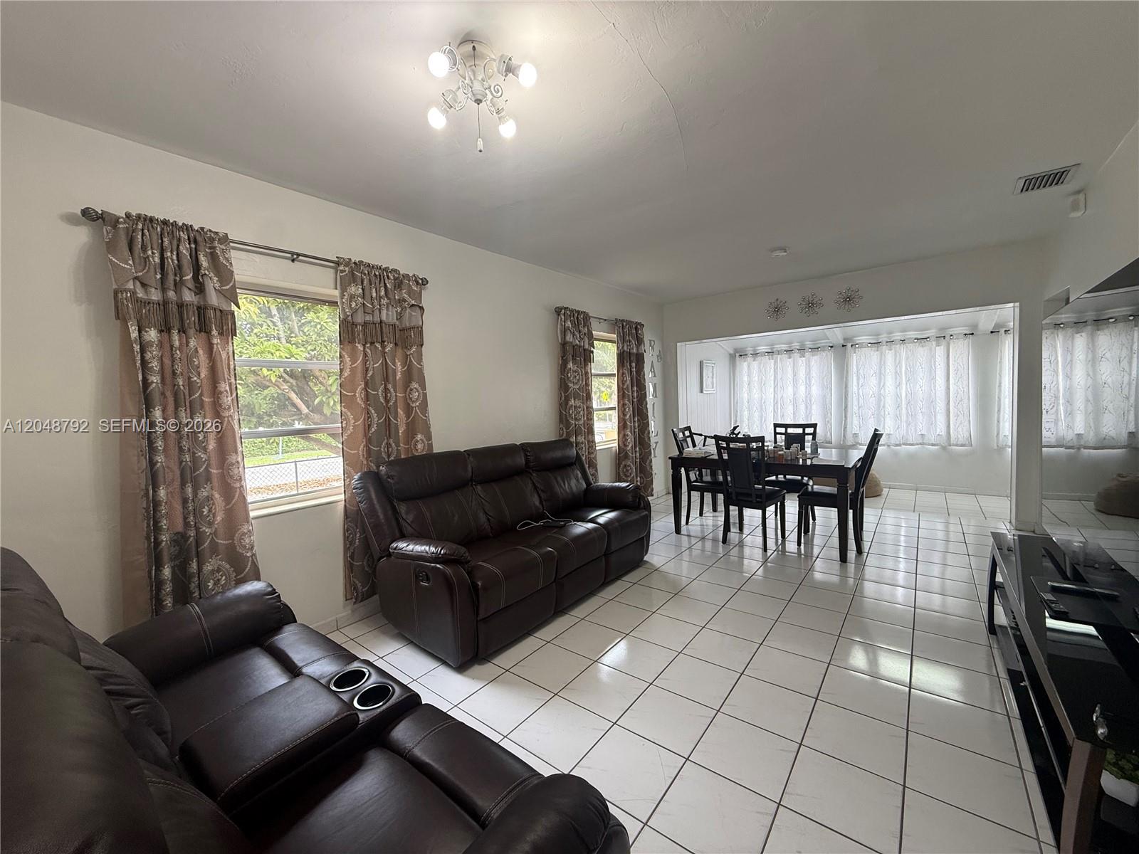 A living and dining area features white tile floors, dark leather furniture, and patterned curtains — 4470 W 1st Ave, Hialeah FL 33012, HIALEAH, FL