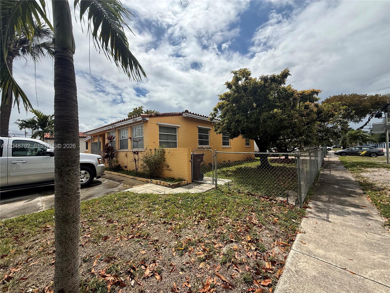 A yellow single-story house with a chain-link fence and a large tree in the yard — 4470 W 1st Ave, Hialeah FL 33012, HIALEAH, FL