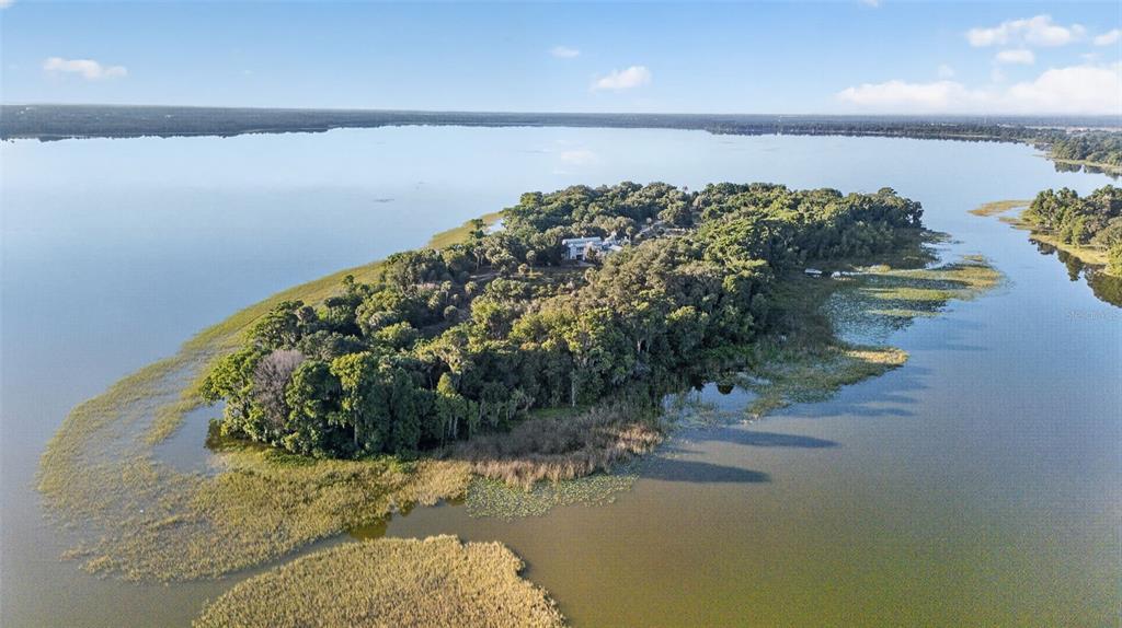 An aerial view shows a house nestled within a wooded island surrounded by a lake — 7950 BANNON FISH CAMP ROAD, HAINES CITY, FL