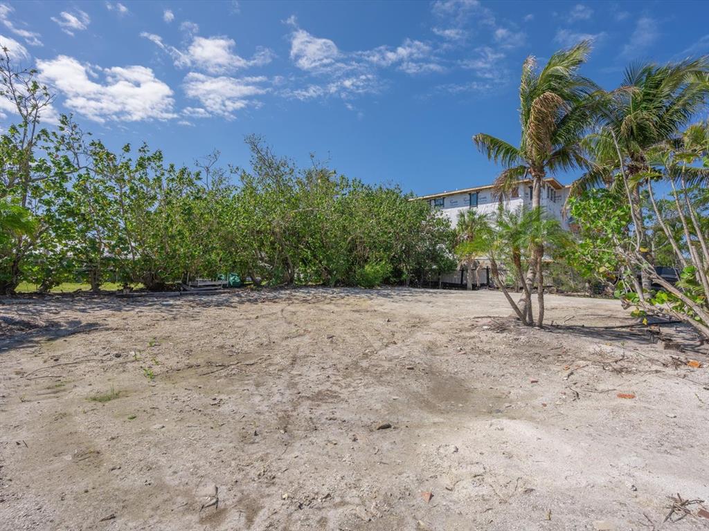 A sandy, undeveloped lot with scattered trees and a building under construction in the background — 720 BROADWAY STREET, LONGBOAT KEY, FL