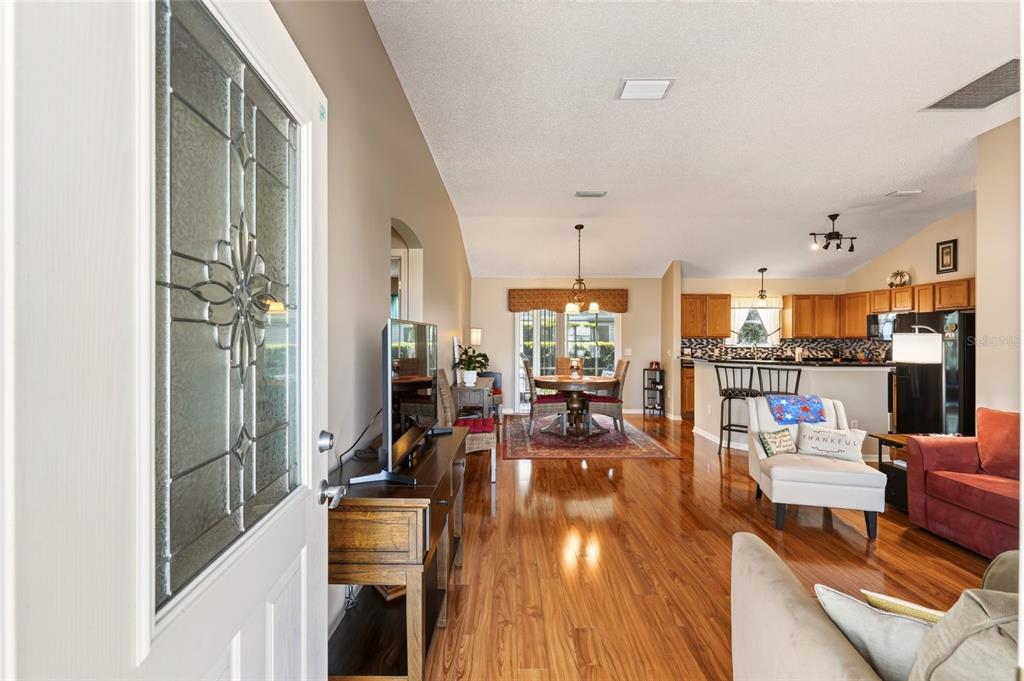 An open-concept living and dining area with hardwood floors, a kitchen, and a front door — 1952 ARDMORE WAY, THE VILLAGES, FL