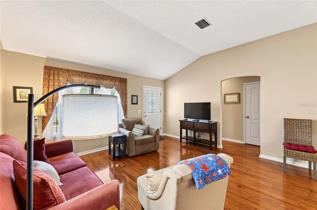 A living room features hardwood floors, a vaulted ceiling, a television console, and multiple chairs — 1952 ARDMORE WAY, THE VILLAGES, FL