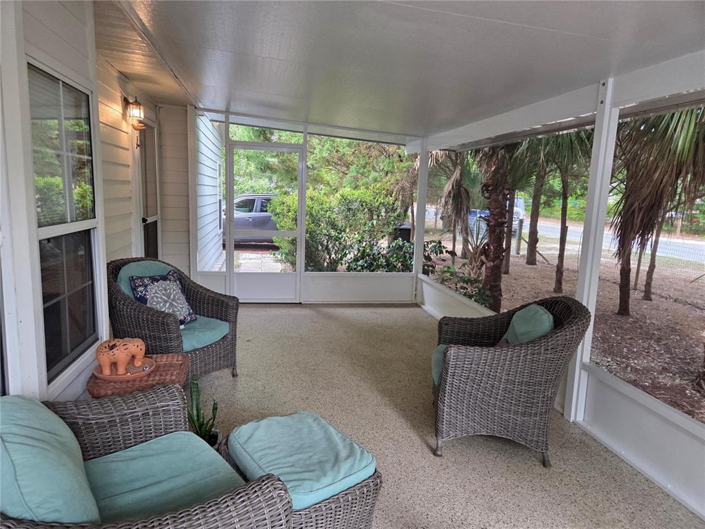 A screened-in porch features wicker furniture, light-colored flooring, and views of trees and a car — 421 MARGARET STREET, BRONSON, FL