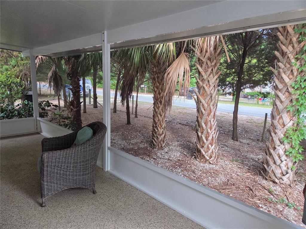 A screened-in porch features a wicker chair, speckled flooring, and views of palm trees — 421 MARGARET STREET, BRONSON, FL