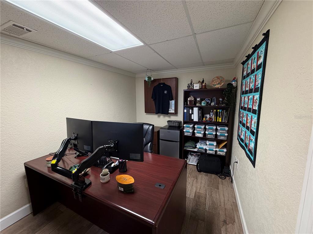 A home office features a dark wood desk, dual monitors, a bookshelf, and a wall quilt — 1302 W BUSCH BOULEVARD, TAMPA, FL