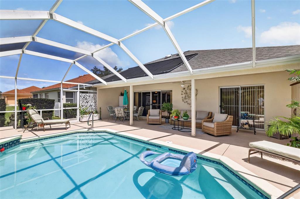 A swimming pool with a screened enclosure sits on a patio next to a house — 1808 SANTANA WAY, THE VILLAGES, FL