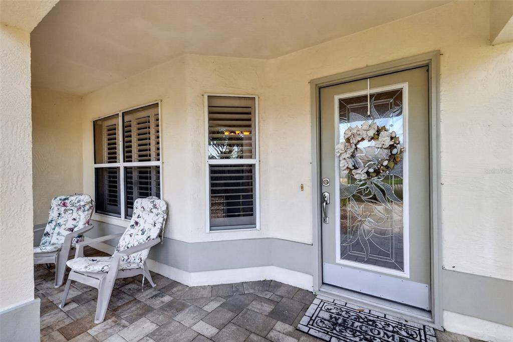 A covered front porch features two chairs, a glass-paneled door, and a welcome mat — 1808 SANTANA WAY, THE VILLAGES, FL
