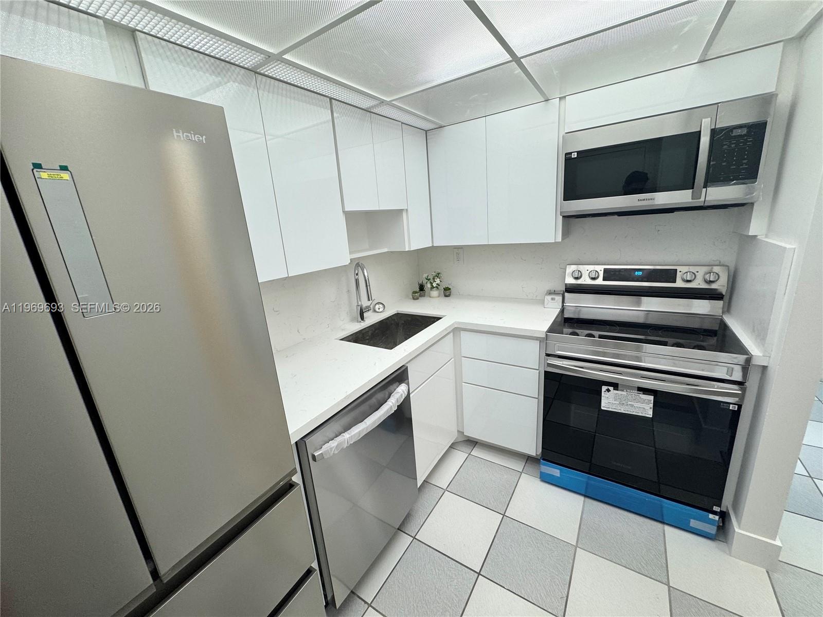 A modern kitchen features white cabinets, stainless steel appliances, and light-colored tiled flooring — 2899 Collins Ave # 740, Miami Beach FL 33140, MIAMI BEACH, FL