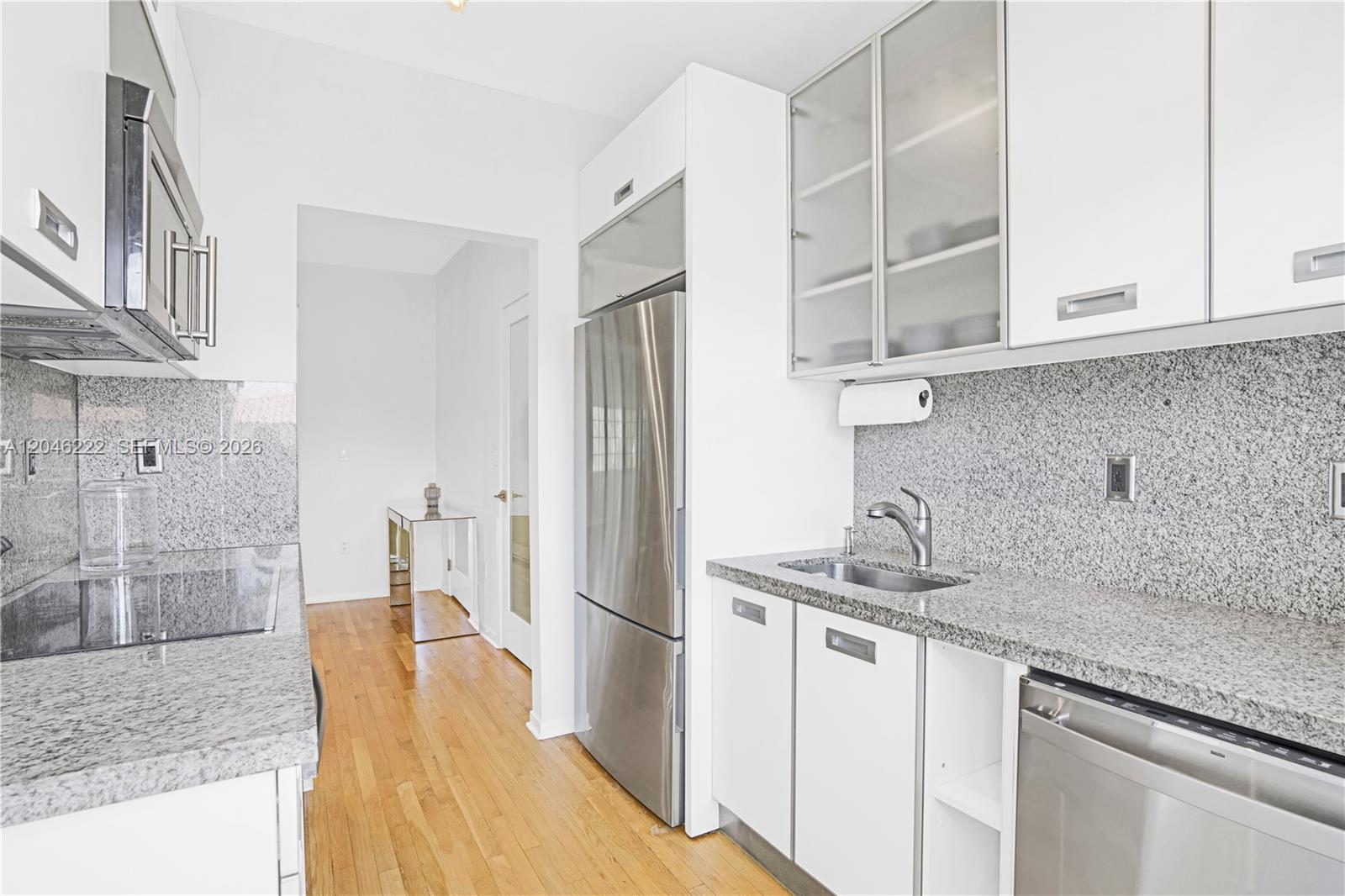 A modern kitchen features white cabinetry, stainless steel appliances, and speckled granite countertops — 1600 Michigan Ave # 6, Miami Beach FL 33139, MIAMI BEACH, FL
