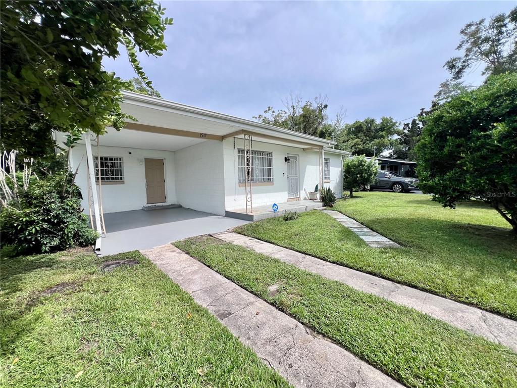 A single-story white house with a carport, concrete driveway, and security bars on the windows — 1517 RILEY AVENUE, ORLANDO, FL
