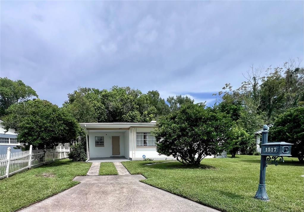 A single-story white house with a concrete driveway and a front lawn under a cloudy sky — 1517 RILEY AVENUE, ORLANDO, FL