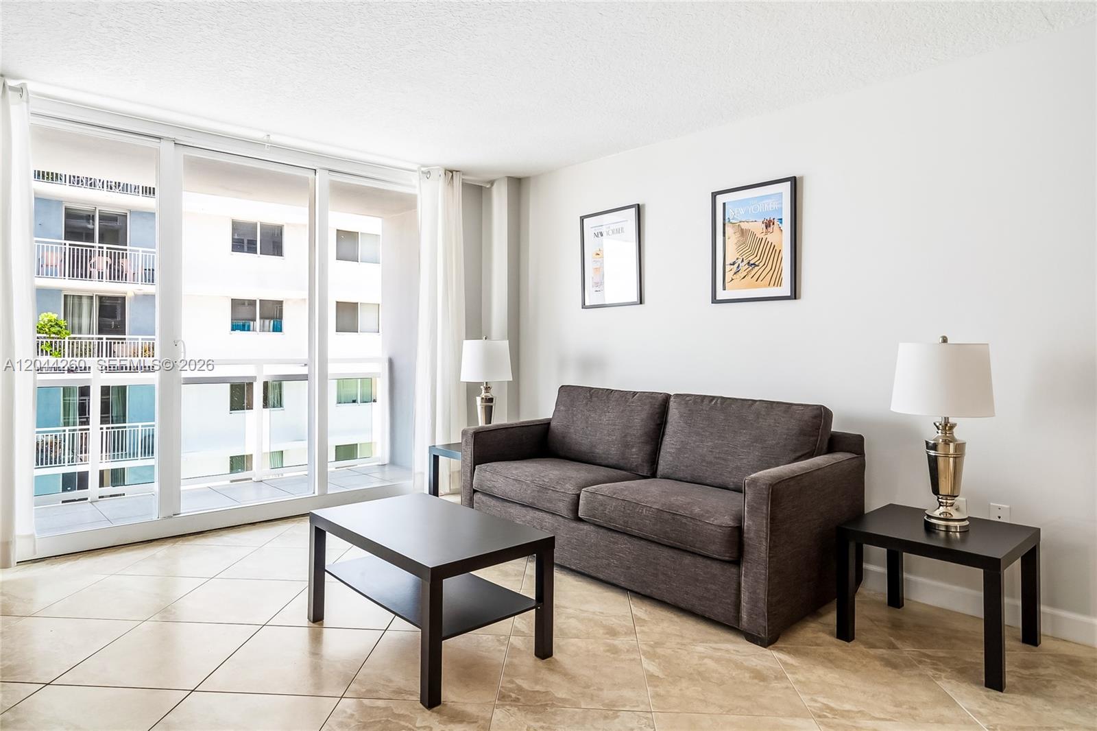 A living room features a dark sofa, a coffee table, two end tables, and balcony access — 6917 Collins Ave # 1012, Miami Beach FL 33141, MIAMI BEACH, FL