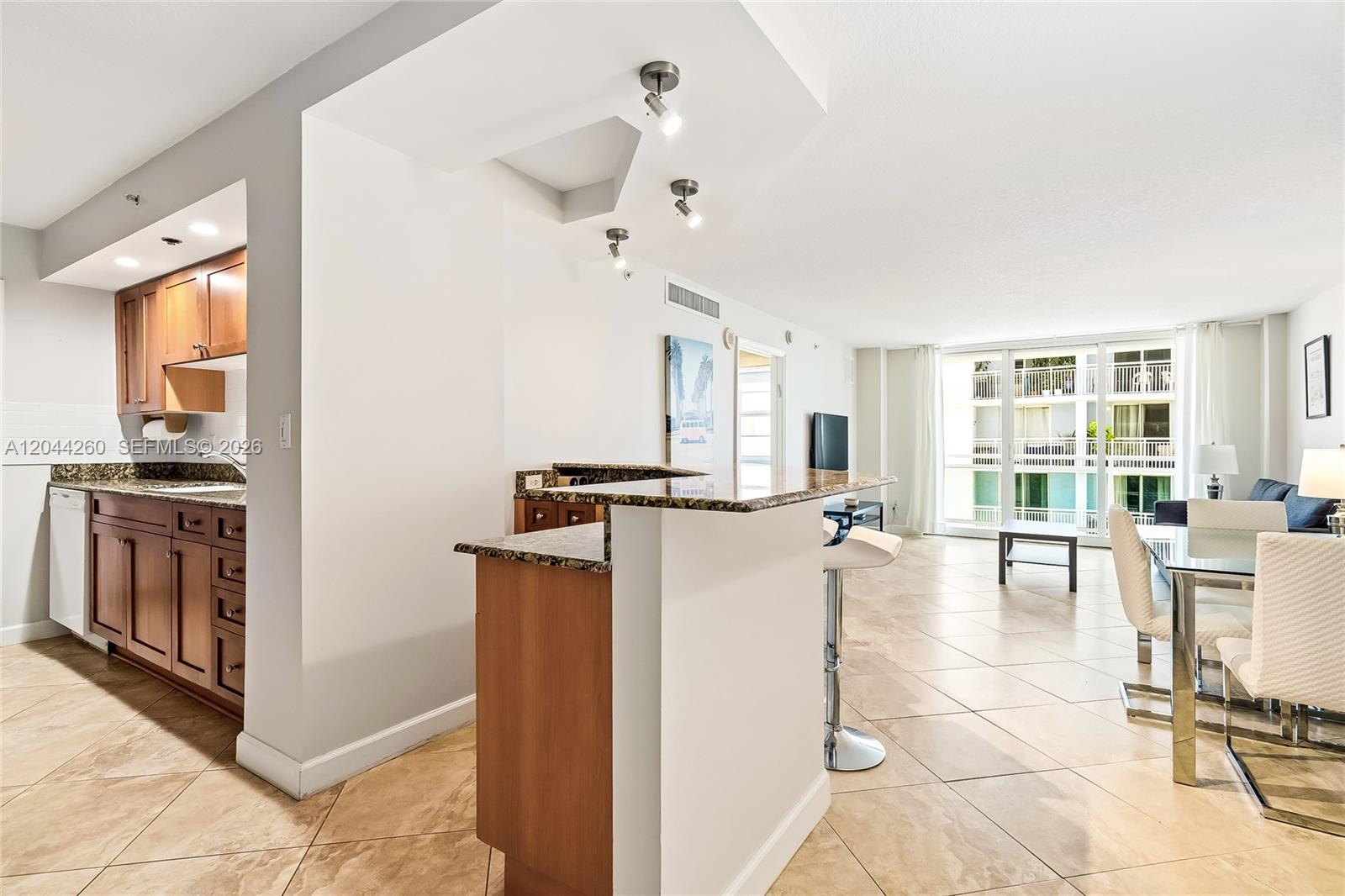 A kitchen with wood cabinets and a breakfast bar opens into a tiled living area — 6917 Collins Ave # 1012, Miami Beach FL 33141, MIAMI BEACH, FL
