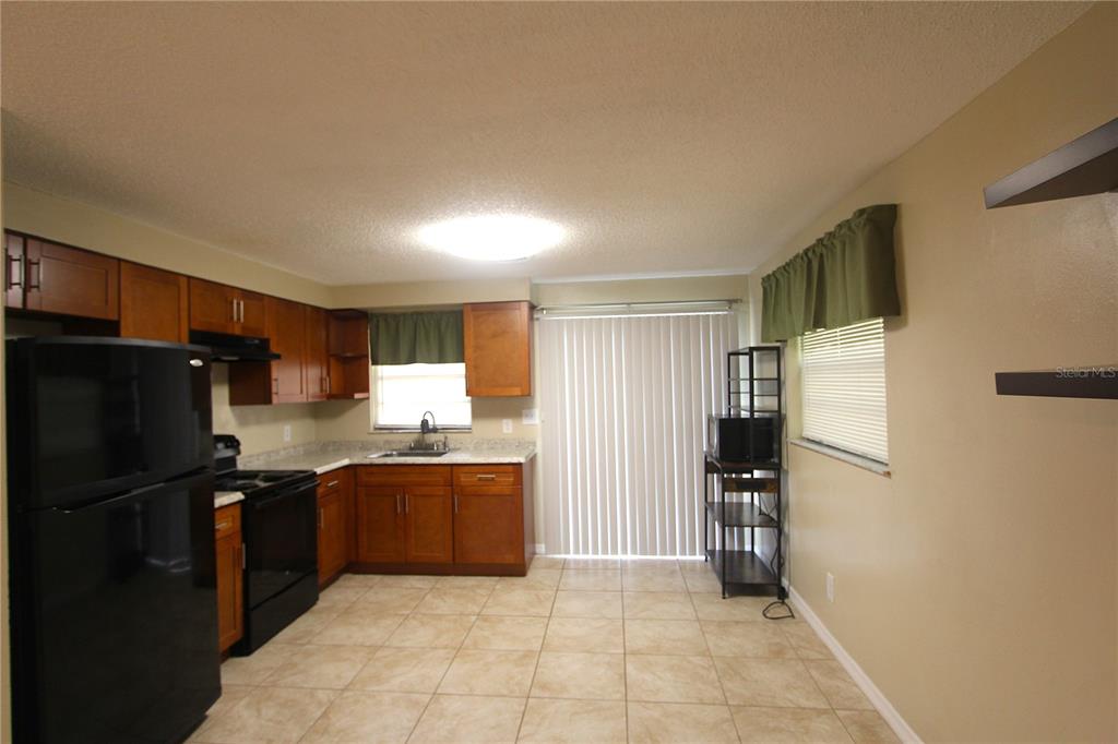 A kitchen features wood cabinets, black appliances, tile flooring, and a sliding glass door — 38942 9TH AVENUE, ZEPHYRHILLS, FL
