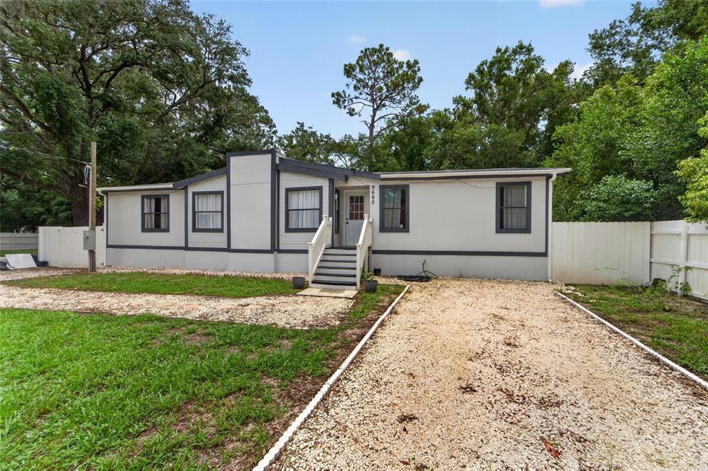 A single-story manufactured home with light gray siding and dark trim sits on a gravel lot — 9690 JEROME DRIVE, NEW PORT RICHEY, FL