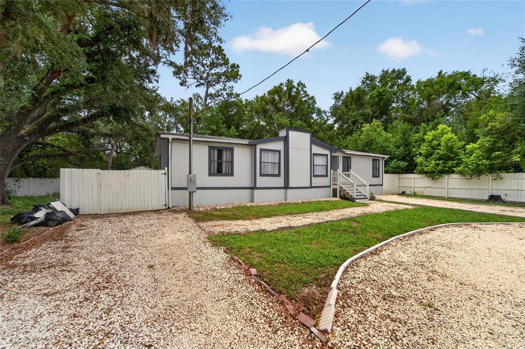 A single-story manufactured home with light gray siding, dark trim, and a gravel driveway — 9690 JEROME DRIVE, NEW PORT RICHEY, FL