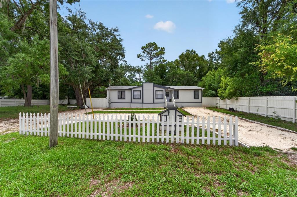 A single-story manufactured home with a gravel driveway and white picket fence in the yard — 9690 JEROME DRIVE, NEW PORT RICHEY, FL