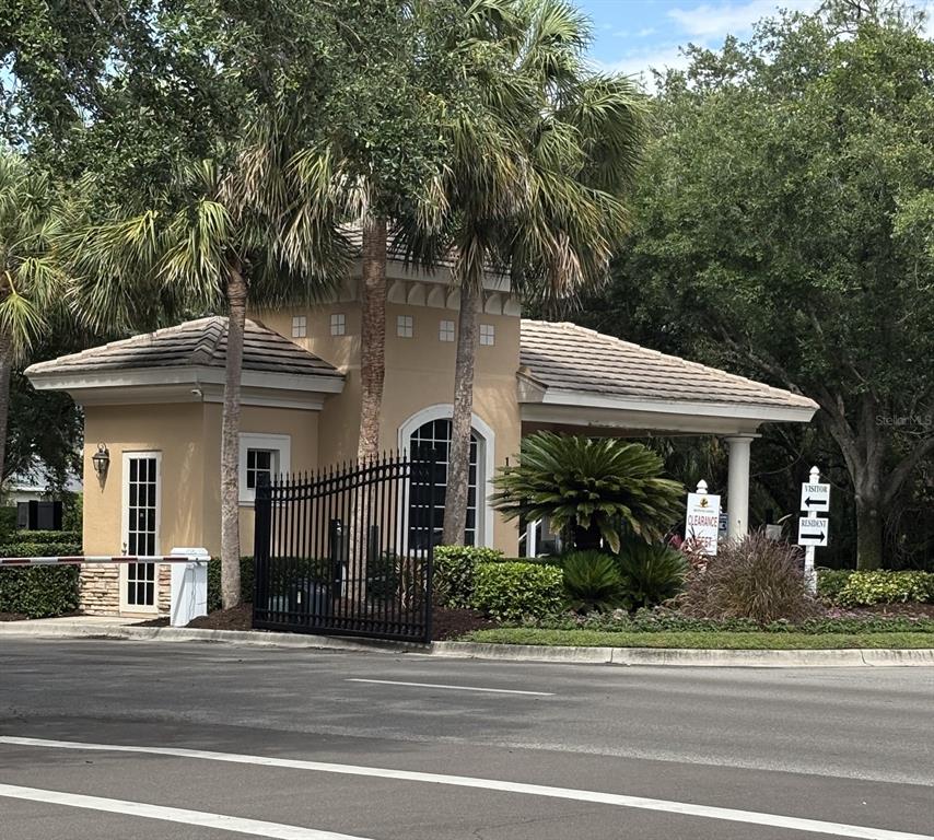 A gated community entrance features a beige guardhouse with a tiled roof and palm trees — 267 PETREL TRAIL, BRADENTON, FL
