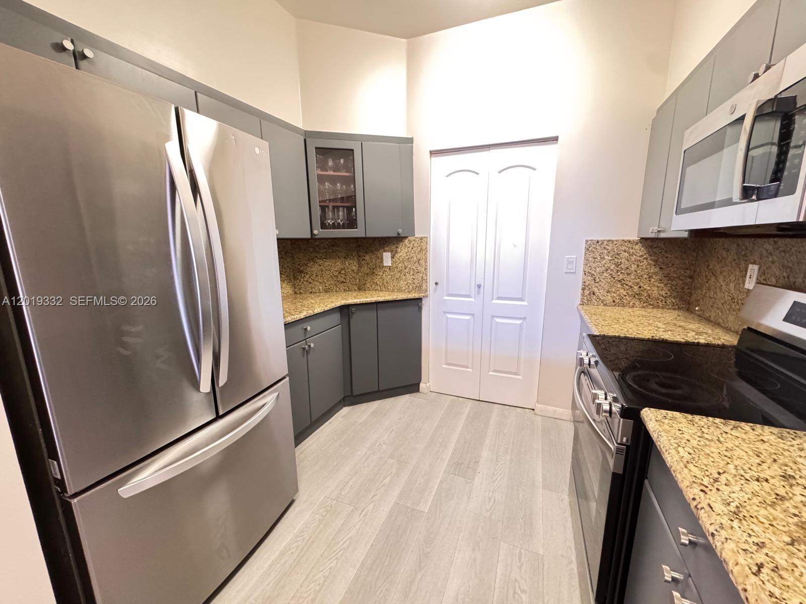 A kitchen features gray cabinets, granite countertops, stainless steel appliances, and light wood-look flooring — 8816 Collins Ave # 206, Surfside FL 33154, SURFSIDE, FL