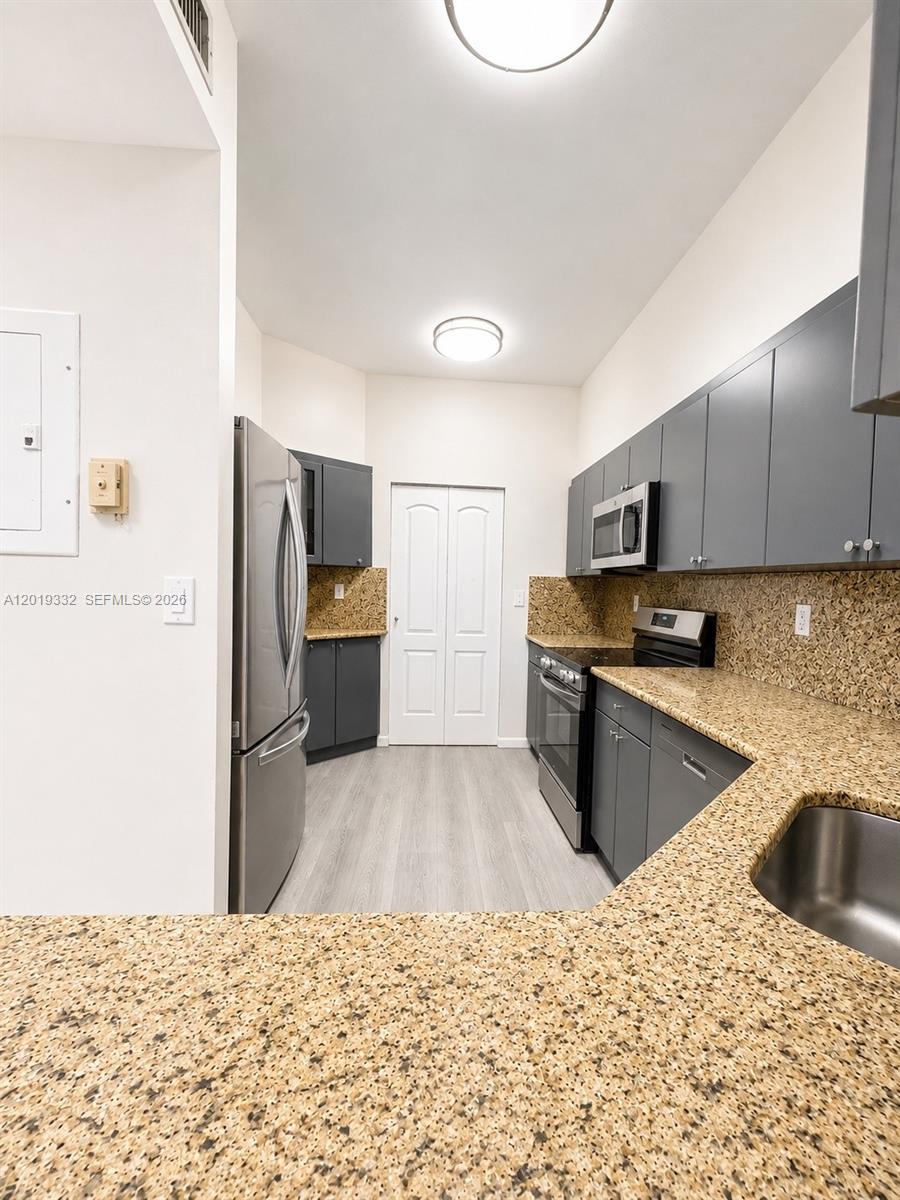 A kitchen features dark gray cabinets, granite countertops, stainless steel appliances, and light wood flooring — 8816 Collins Ave # 206, Surfside FL 33154, SURFSIDE, FL