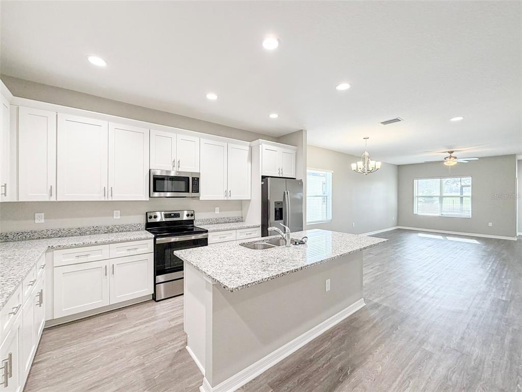 A kitchen with white cabinets, granite countertops, and stainless steel appliances opens to a living area — 3376 CUP DRIVE, LAKELAND, FL