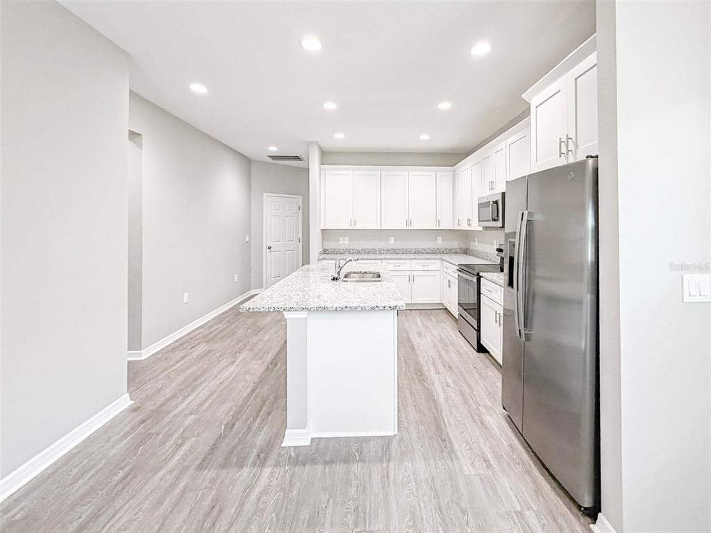 A modern kitchen features white cabinets, granite countertops, a center island, and stainless steel appliances — 3376 CUP DRIVE, LAKELAND, FL