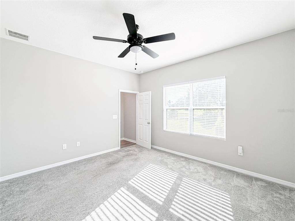 An empty bedroom features gray carpet, light walls, a ceiling fan, and a window with blinds — 3376 CUP DRIVE, LAKELAND, FL