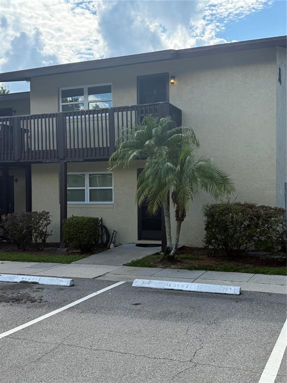 A two-story apartment building exterior features a wooden balcony, a palm tree, and parking spaces — 141 FERNERY ROAD UNIT A204, LAKELAND, FL