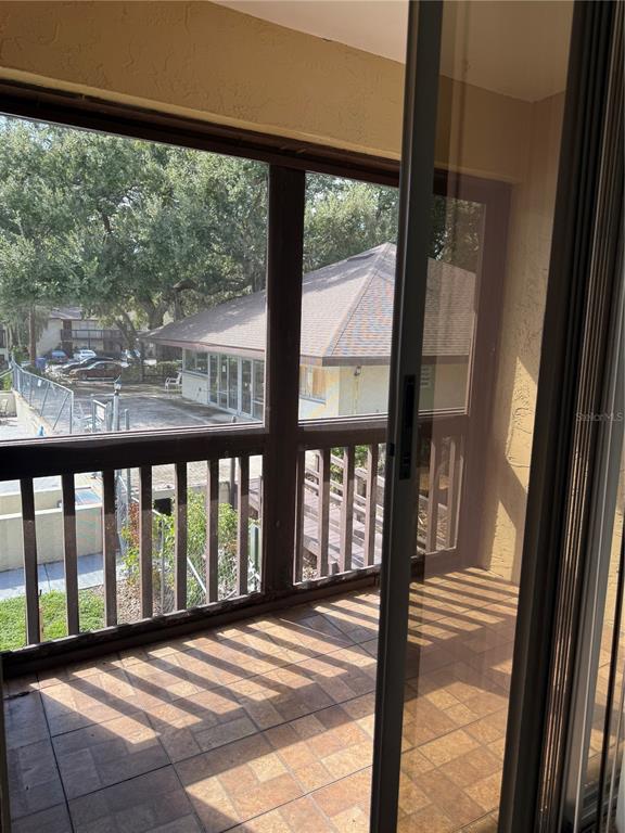 A tiled balcony with a screen enclosure overlooks a neighboring building and parking area — 141 FERNERY ROAD UNIT A204, LAKELAND, FL