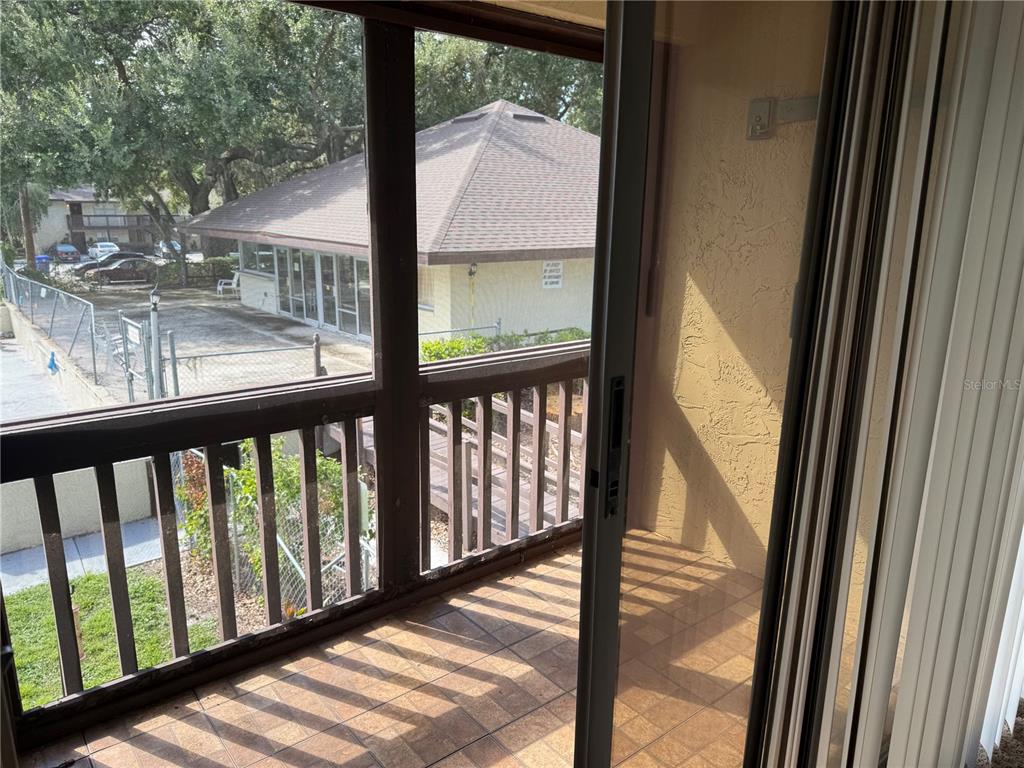 A tiled balcony with a wooden railing overlooks a neighboring building and parking area — 141 FERNERY ROAD UNIT A204, LAKELAND, FL