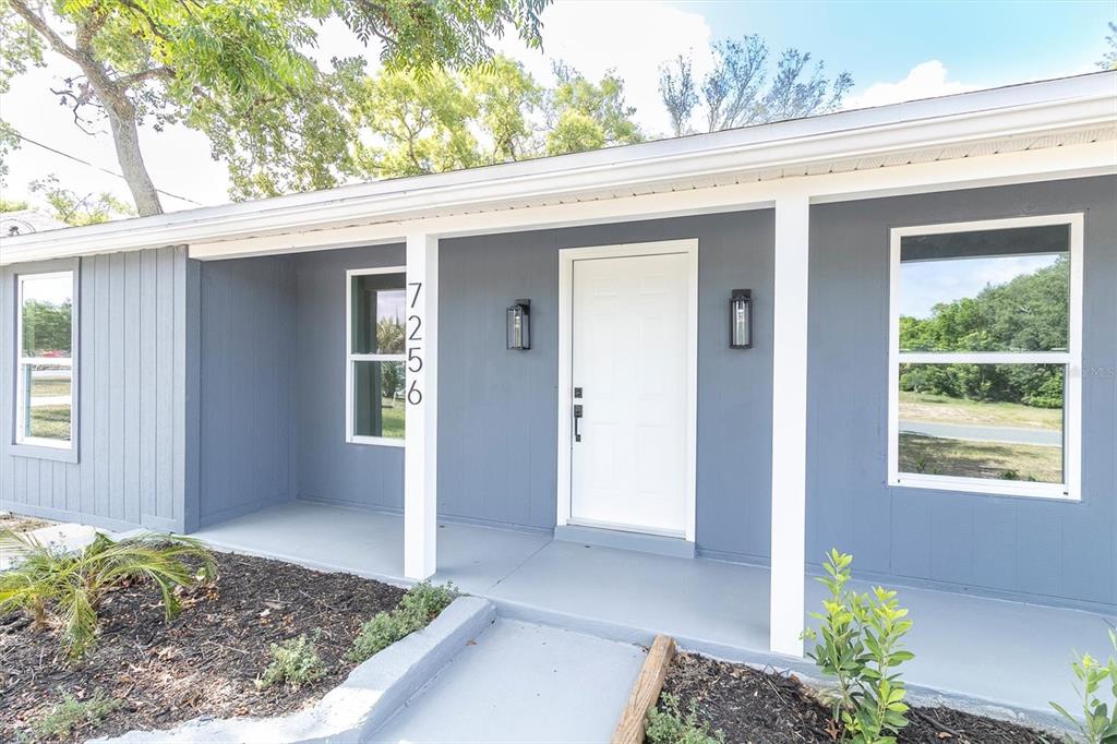 The exterior of a gray house features a white front door and a covered porch — 7256 PINEHURST DRIVE, SPRING HILL, FL