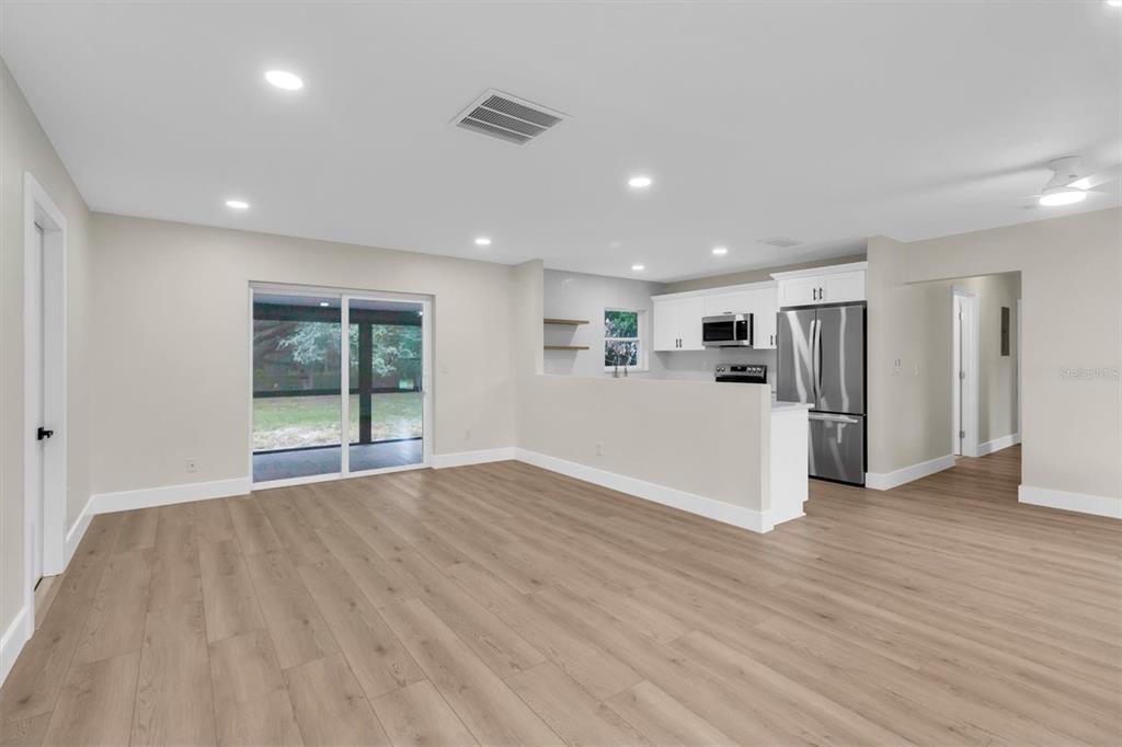 An open-concept living area with light wood-look flooring, recessed lighting, and a kitchen with stainless appliances — 7256 PINEHURST DRIVE, SPRING HILL, FL