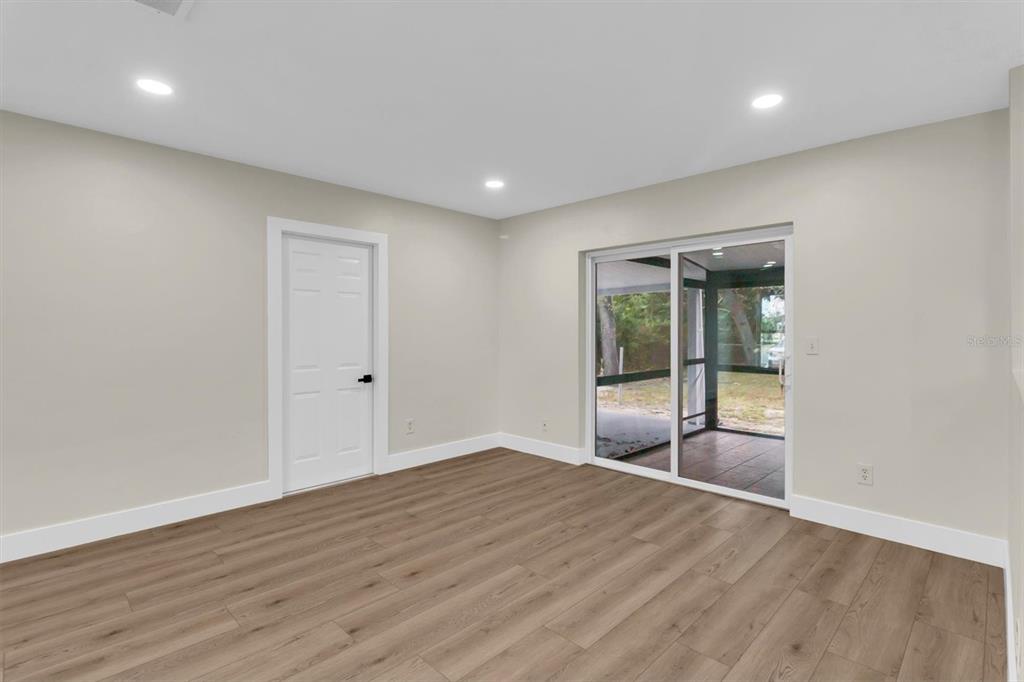 An empty room with light-colored walls, wood-look flooring, a white door, and sliding glass doors — 7256 PINEHURST DRIVE, SPRING HILL, FL