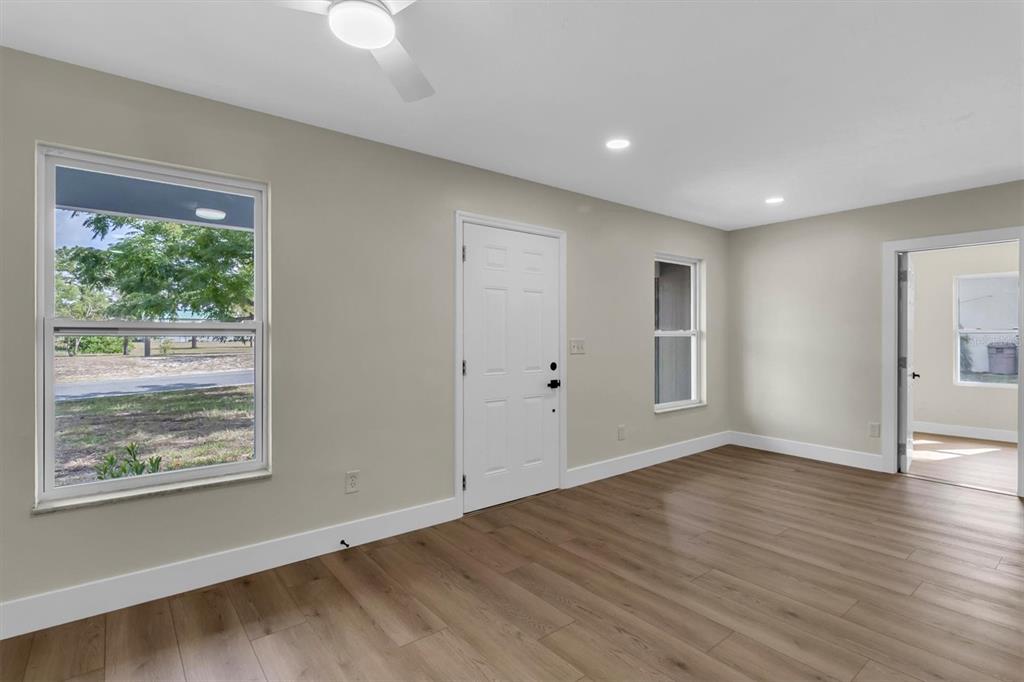 An empty room features light wood-look flooring, beige walls, a white door, and two windows — 7256 PINEHURST DRIVE, SPRING HILL, FL