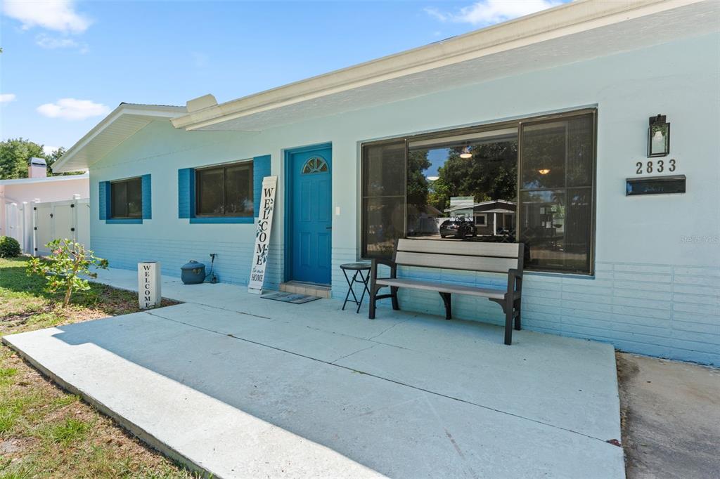 A light blue house exterior features a concrete porch, a blue door, and a bench — 2833 56TH LANE N, ST PETERSBURG, FL