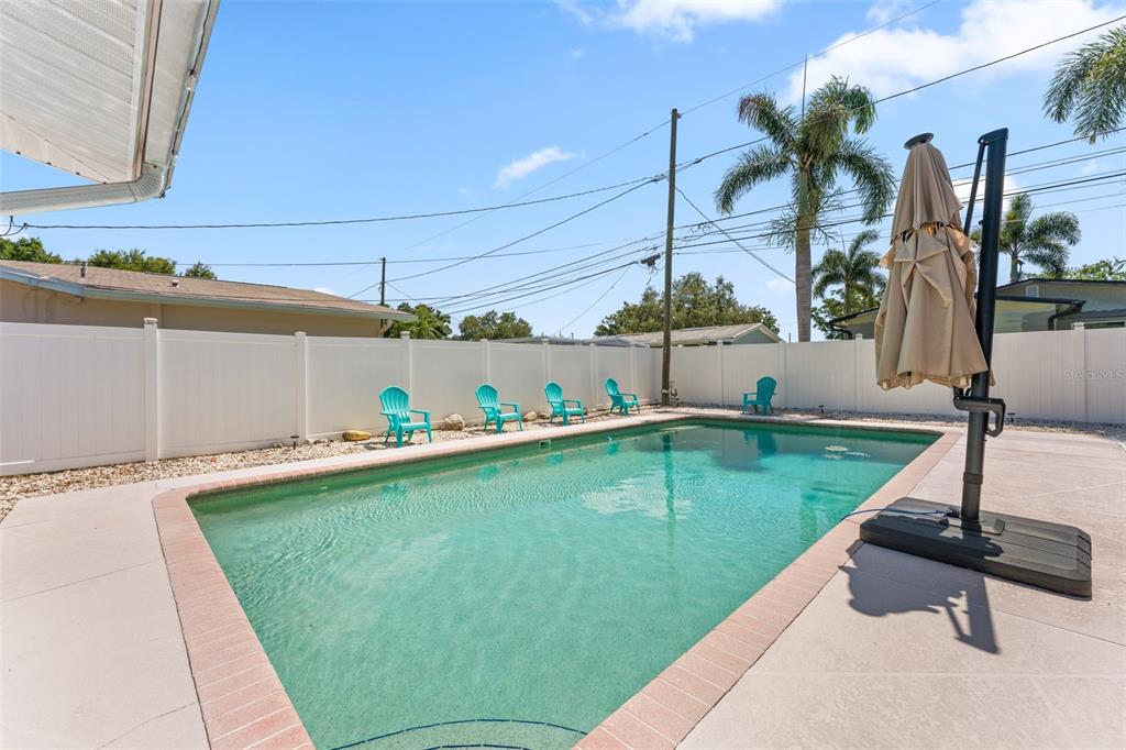 A rectangular swimming pool with a patio and turquoise chairs sits in a fenced backyard — 2833 56TH LANE N, ST PETERSBURG, FL