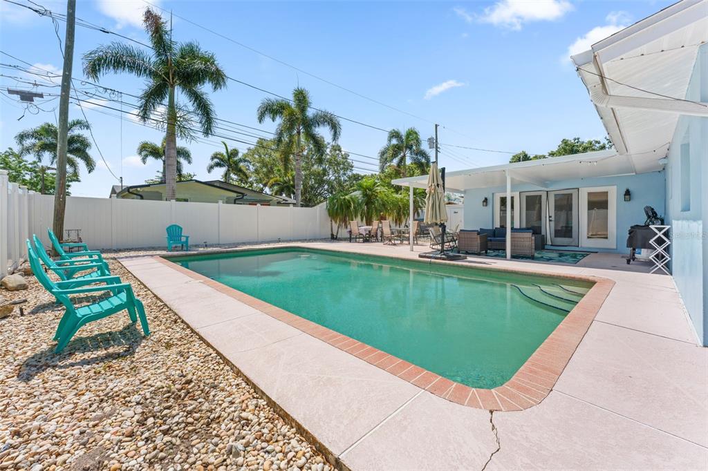 A backyard features a rectangular swimming pool, a covered patio, and several turquoise lounge chairs — 2833 56TH LANE N, ST PETERSBURG, FL