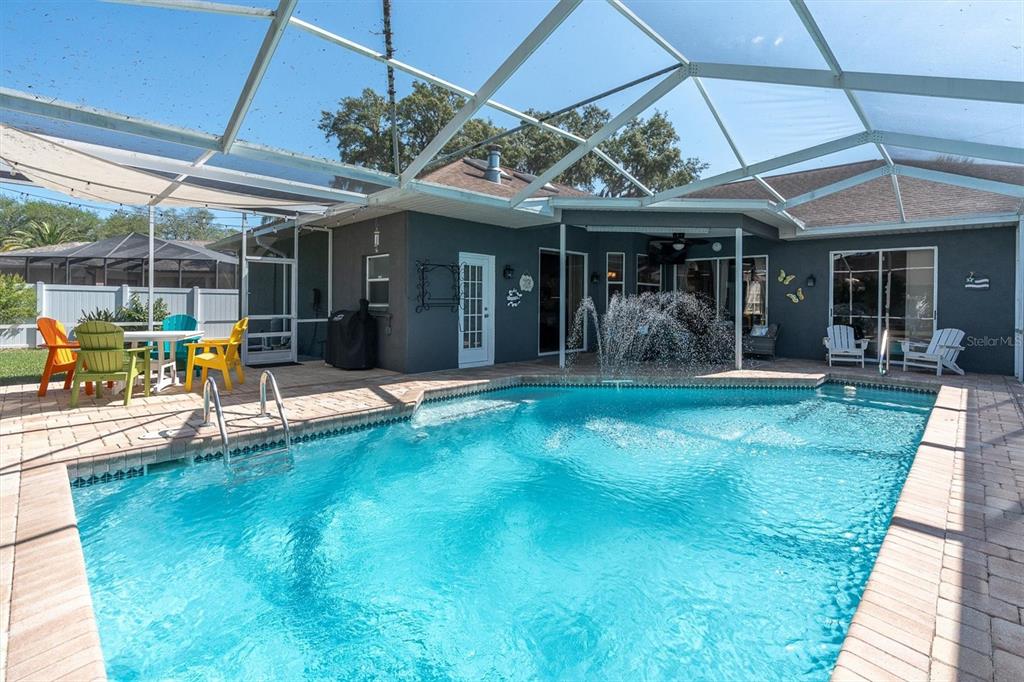 A swimming pool with a fountain sits inside a screened-in patio behind a house — 4851 DEER LODGE ROAD, NEW PORT RICHEY, FL