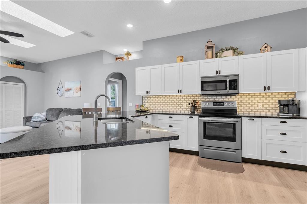 A modern kitchen features white cabinets, a dark granite island, and stainless steel appliances — 4851 DEER LODGE ROAD, NEW PORT RICHEY, FL