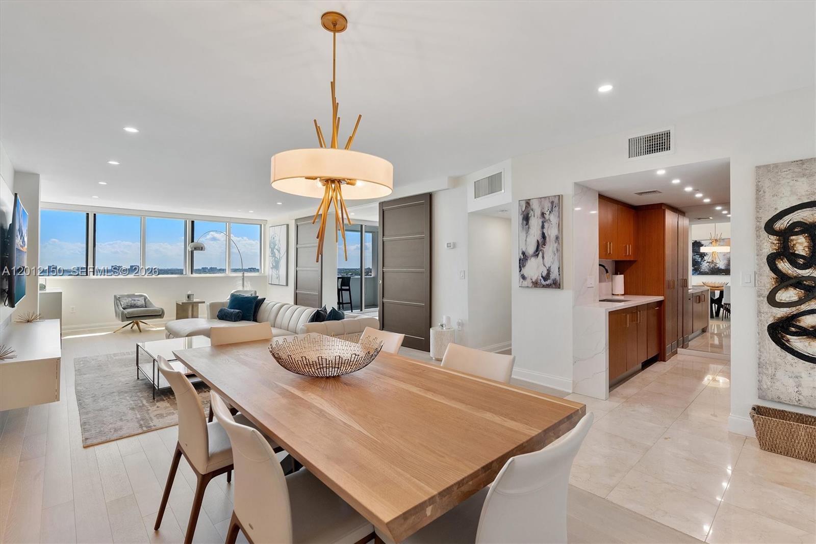 A dining area with a wooden table and modern chandelier opens to a living room — 10275 Collins Ave # 1530, Bal Harbour FL 33154, BAL HARBOUR, FL