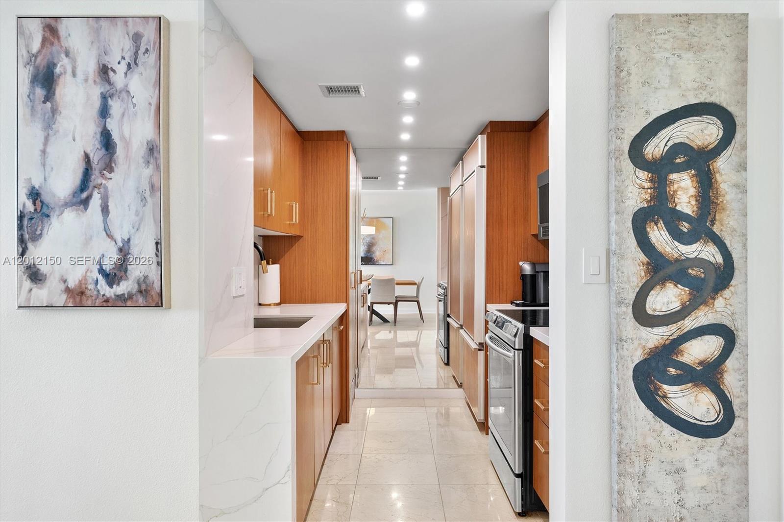 A galley kitchen features wood cabinetry, white marble countertops, and stainless steel appliances — 10275 Collins Ave # 1530, Bal Harbour FL 33154, BAL HARBOUR, FL