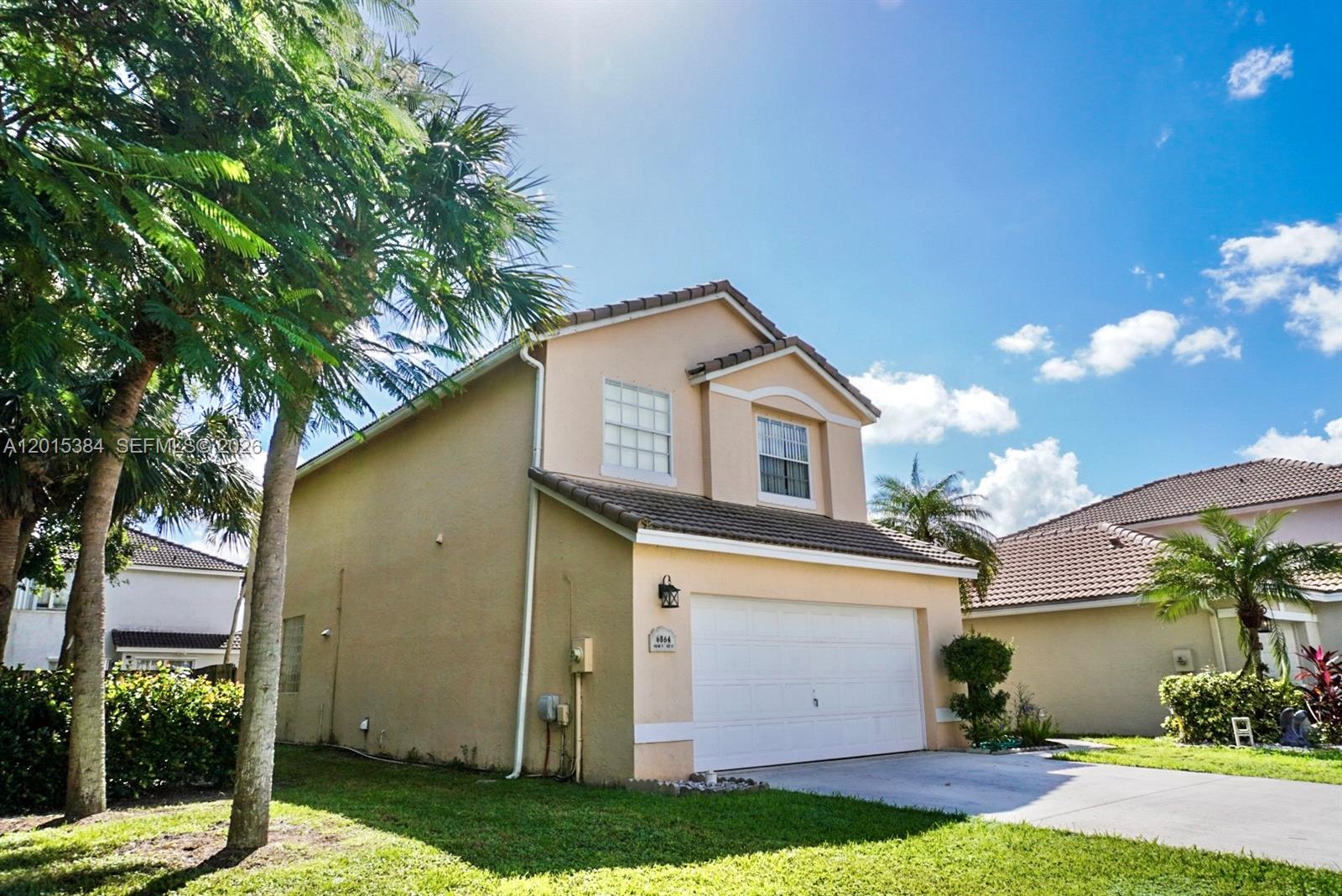 A two-story beige house features a white garage door and a palm tree in front — 6864 Sugarloaf Key St, Lake Worth FL 33467, LAKE WORTH, FL