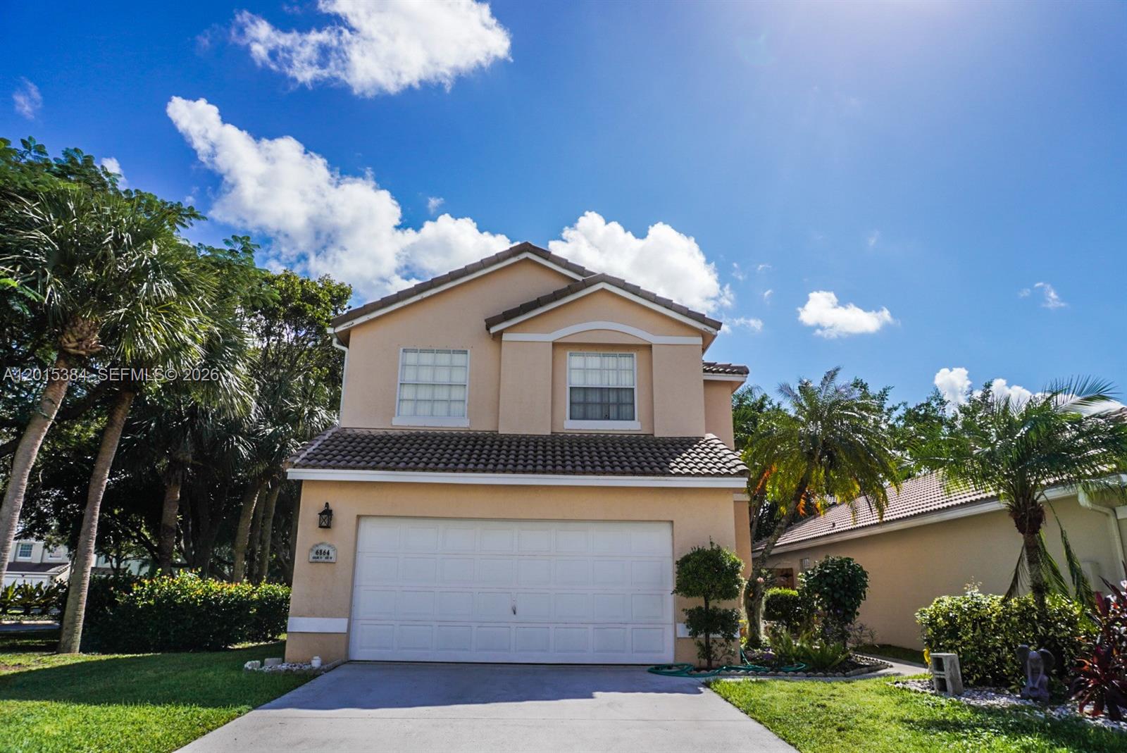 A two-story tan house features a white garage door and a tiled roof — 6864 Sugarloaf Key St, Lake Worth FL 33467, LAKE WORTH, FL