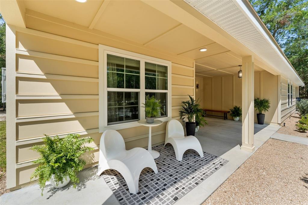 A covered porch features two white chairs, a small table, and potted plants — 9580 US 27 ALT, BRONSON, FL
