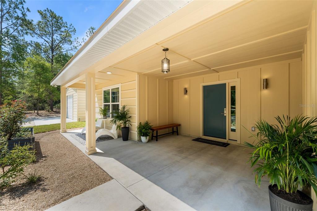 A covered concrete porch features a teal front door, a wooden bench, and potted plants — 9580 US 27 ALT, BRONSON, FL