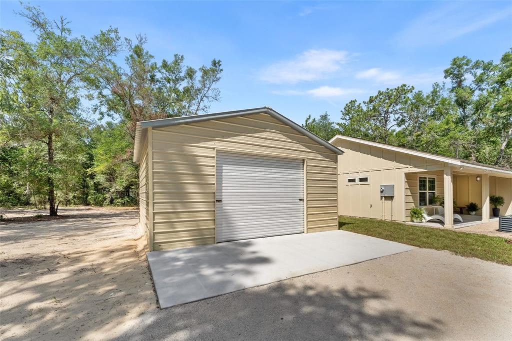 A detached metal garage with a roll-up door sits on a concrete pad next to a house — 9580 US 27 ALT, BRONSON, FL