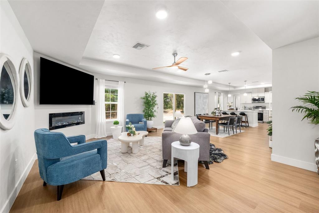 An open-concept living and dining area features light wood floors, a fireplace, and blue chairs — 9580 US 27 ALT, BRONSON, FL