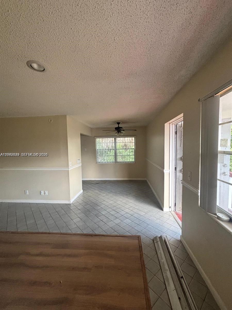 A room with beige walls, a popcorn ceiling, and gray tile flooring leads to a window — 280 Northampton, West Palm Beach FL 33417, WEST PALM BEACH, FL